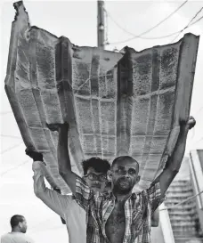  ?? CARLOS GIUSTI, AP ?? Residents from La Perla carry a piece of metal through the streets of San Juan on Monday.