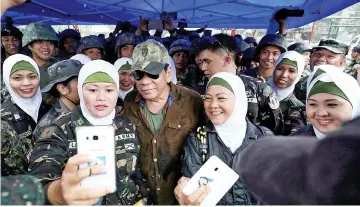  ??  ?? Duterte (centre) poses for a picture with female soldiers during his visit at Bangolo town in Marawi city, southern Philippine­s. — Reuters photo