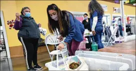  ?? HYOSUB SHIN/ HYOSUB. SHIN@ AJC. COM ?? Gwinnett County Public Schools’ Hispanic Mentoring Program staff Tania Muniz ( foreground) hands out a bag of two science experiment­s and Christmas gif t to parent Eloisa Caricia ( lef t) at Plaza Las Americas.