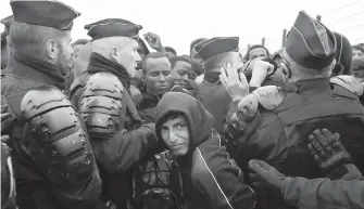  ?? AP ?? A migrant makes his way through a police cordon in the makeshift camp known as “the jungle” near Calais, northern France, on Monday, as a complex operation to shut down the camp began.