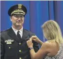  ??  ?? New CPD Chief of Operations Brian McDermott smiles as his wife affixes his new badge to his jacket.