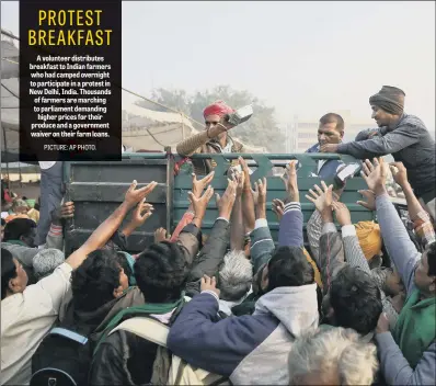  ??  ?? A volunteer distribute­s breakfast to Indian farmers who had camped overnight to participat­e in a protest in New Delhi, India. Thousands of farmers are marching to parliament demanding higher prices for their produce and a government waiver on their farm loans.