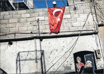  ?? Photo: Yasin Akgul/AFP ?? Defiant: A man hangs a Turkish flag on top of his house, which was damaged by rockets fired from an area in Syria controlled by the Islamic State. The city of Kilis has taken in many refugees.