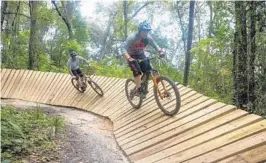  ??  ?? Shawn Lukens, owner of Adrenaline BikeWorks, front, rolls along a wooden bermwhile the shop’s service manager, Joey Hill, follows on the Mount Dora mountain bike trails.