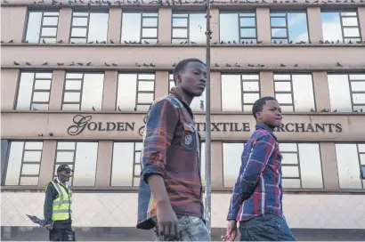  ?? Picture: Yeshiel Panchia ?? Men walk past the Golden Glow Textile Merchants’ building on Lillian Road in Fordsburg, Johannesbu­rg, this week.