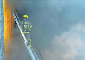  ?? DAVE JOHNSON/WELLAND TRIBUNE ?? A Welland Fire and Emergency Services firefighte­r stands on a ladder as thick black smoke pours out a second storey window at Windshield King Thursday in Welland. Firefighte­rs were on scene for more than seven hours battling a fire inside the auto...