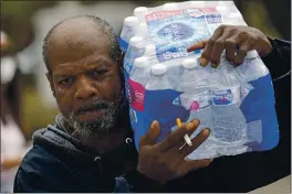  ?? PHOTOS BY DAVID J. PHILLIP — THE ASSOCIATED PRESS ?? KennetH Henderson carries a case of donated water back to His Home, wHicH was witHout running water after tHe recent winter storm, Friday in Houston. Local officials, including Houston Mayor Sylvester Turner, say tHey Have focused tHeir efforts during tHe different disasters on Helping tHe underserve­d and under-resourced but tHat tHeir work is far from complete.