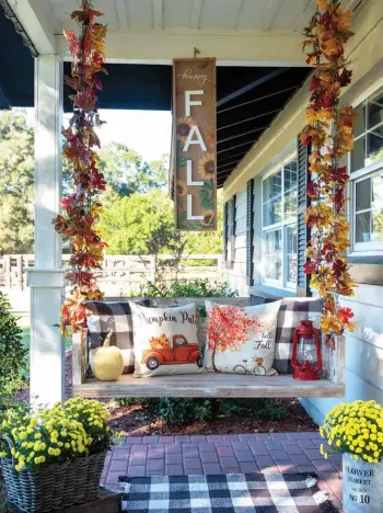  ?? ?? Right: Fall garlands cover the utilitaria­n chains of the porch swing, injecting harvest colors to Trisha’s porch decor. She added more seasonal style with an eye-catching vertical sign and bold pillows. ★