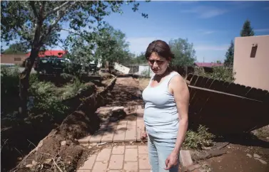  ?? PHOTOS BY OLIVIA HARLOW/THE NEW MEXICAN ?? Gladys Trujillo stands in her yard following Monday night’s flash flood. Trujillo was in Pojoaque with family when the storm started, and when she came home around 9:30 p.m., the 5-foot brick wall that once stood, at left, was gone, and her home flooded.