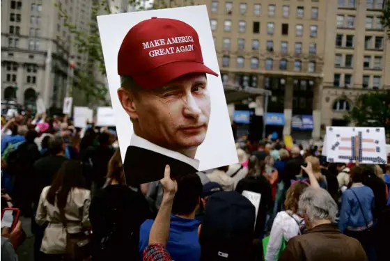  ?? —AP ?? A demonstrat­or holds up a placard with a picture of Russian leader Vladimir Putin winking as he wears a cap made famous by US President Donald Trump during his campaign to “Make America Great Again.”