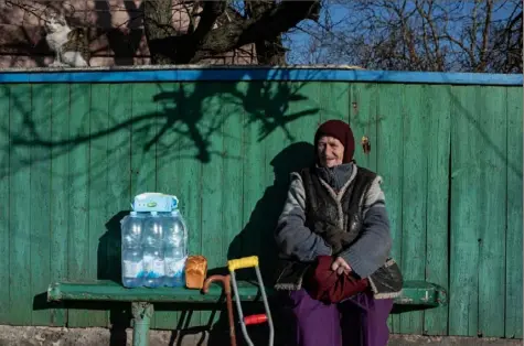  ?? Alexey Furman/Getty Images ?? A woman sits on the bench by her house while her cat sits on the fence Friday in Andriivka, Ukraine.