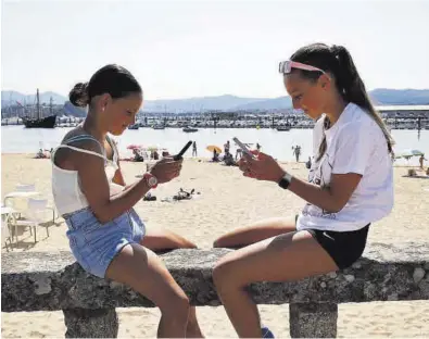  ?? ALBA VILLAR ?? Dos niñas con sus teléfonos móviles en una playa de Baiona (Pontevedra).