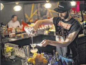  ??  ?? Bartender Keith Baker mixes a Christmapo­litan, which is made of vodka, elderflowe­r, dry vermouth, spiced cranberry sauce, rosemary, lime and absinthe mist.