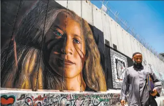  ?? Ahmad Gharabli / AFP / Getty Images ?? A Bethlehem resident passes a mural painted on Israel’s controvers­ial separation barrier in the West Bank depicting Palestinia­n teenager Ahed Tamimi, a prominent protester.