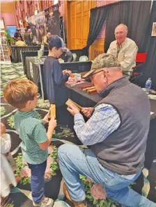  ?? CONTRIBUTE­D PHOTO ?? Jim Clay, top right, works with young turkey callers during the Wild & Wonderful Hunting, Fishing & Conservati­on Expo last weekend at the Greenbrier Resort in White Sulphur Springs, W.Va. “Guns & Cornbread” columnist Larry Case, foreground right, also enjoyed his visit to Clay’s booth and tried out some of the calls himself.