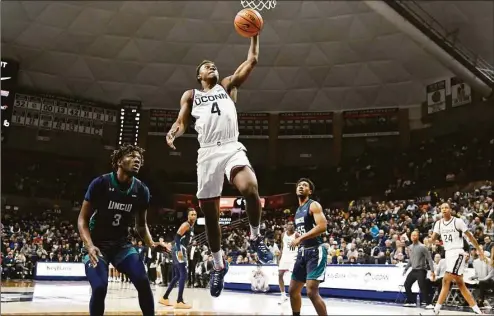  ?? Jessica Hill / Associated Press ?? UConn’s Nahiem Alleyne (4) dunks as UNC-Wilmington’s Maleeck Harden-Hayes looks on during a Nov. 18 game in Storrs.