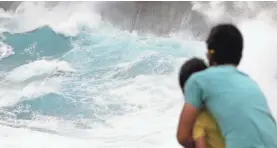  ?? CALEB JONES/AP ?? A man and his son watch waves crash off sea cliffs last August.