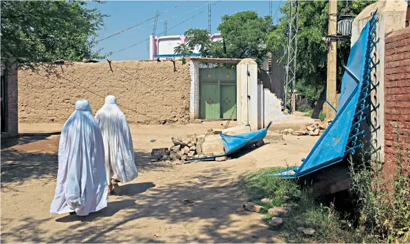  ??  ?? Women pass the remains of the health clinic in Masho Khel in northern Pakistan after the mob’s attack