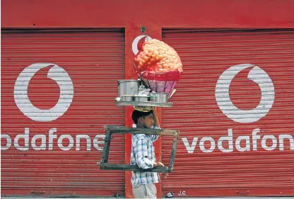  ?? /Reuters ?? Competitiv­e market: A vendor selling ’paani puri’, a traditiona­l Indian snack, walks past closed shops displaying an advertisem­ent for Vodafone in Jammu in May 2012. A Vodafone and Idea Cellular merger would create an operator with 387-million...