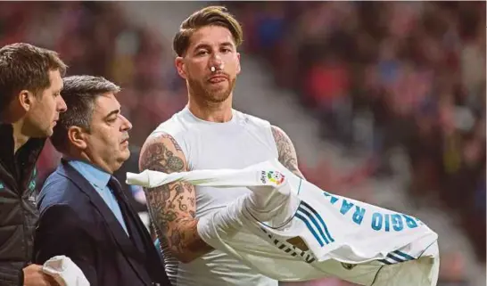  ?? [ FOTO EFE ] ?? Ramos diiringi pasukan perubatan selepas patah tulang hidung ketika menentang Atletico Madrid, kelmarin.