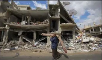  ?? HASSAN AMMAR - THE ASSOCIATED PRESS ?? In this 2016 photo, a Syrian man carries a carpet through a devastated part of the town of Palmyra as families load their belongings onto buses in the central Homs province in Syria. Syrian media says a pair of attacks on two security locations in the...