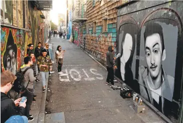  ?? KARL MONDON/STAFF ?? A crowd gathers to watch Mel Waters paint a mural of Ghost Ship fire victims Alex Vega and Michela Gregory.