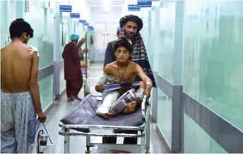  ?? — AFP photo ?? A man pushes an injured boy on a stretcher along a hospital corridor in Kandahar, as he receives medical treatment after being hurt by a roadside bomb that struck a bus overnight killing at least 11 people.