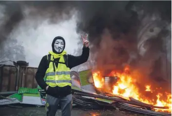  ?? — AFP ?? A protester wearing a Guy Fawkes mask makes the victory sign near a burning barricade during a protest of Yellow vests (Gilets jaunes) against rising oil prices and living costs in Paris.
