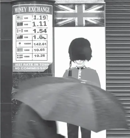 ?? Associated Press file photo ?? ABOVE:
A pedestrian with an umbrella passes a board on Jan. 16 showing the exchange rates at a money exchange bureau in London. If you’re planning an overseas trip this year, experts have advice for saving money, getting decent exchange rates and...