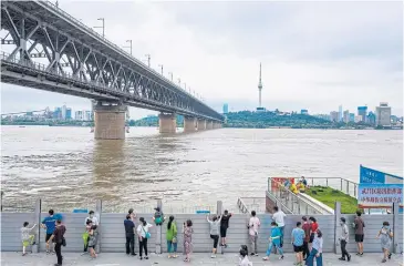  ?? AFP ?? Residents observe the swollen Yangtze River over an anti-flood wall in Wuhan in China’s central Hubei province on Sunday.