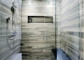  ??  ?? Modern with a hint of rustic, the guest bathroom in the Staples home turns the custom shower into a focal point. It includes a built-in bench, rain shower head, black river-rock tiles for visual interest and a sense of warmth in the random-pattern wood...