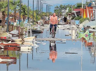  ?? GIANNIS MOISIADIS THE ASSOCIATED PRESS ?? A man rides a bicycle among debris after a storm at Nea Plagia village in Halkidiki region, northern Greece, Thursday. A powerful storm hit the northern Halkidiki region late Wednesday.