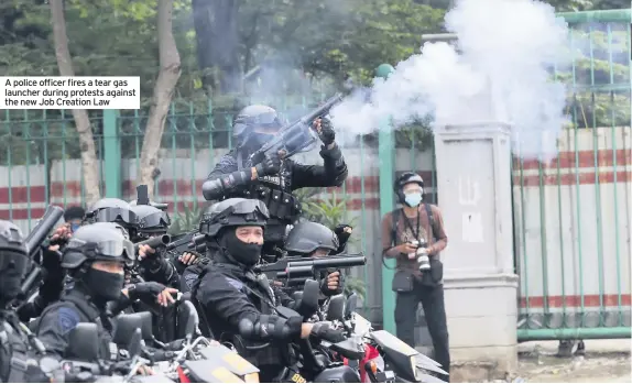  ??  ?? A police officer fires a tear gas launcher during protests against the new Job Creation Law