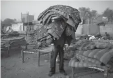  ?? KEVIN FRAYER/AP ?? A worker carries a pile of blankets rented by Indian squatters early in the morning at Park No. 2 in New Delhi. Hours later, cars reoccupy the park.