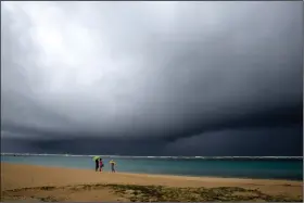  ?? (AP/Caleb Jones) ?? People hold umbrellas as it begins to rain on an otherwise empty beach Monday in Honolulu.