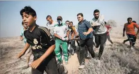  ?? MOHAMMED SABER/EPA ?? Palestinia­n youths carry a comrade injured in clashes with Israeli troops near the border with Israel after a protest against the security measures at a shrine in Jerusalem.