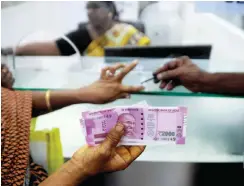  ??  ?? CHENNAI: An Indian woman holds INR 2000 notes as she has her finger marked with indelible ink after exchanging 500 and 1000 banknotes at a bank in Chennai. — AFP