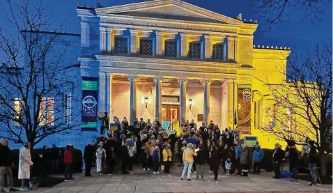  ?? Betsy McMahon/Contribute­d photo ?? Branford residents “stand with Ukraine” last year on the steps of Blackstone Library, lit up in the colors of Ukraine.