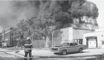  ?? NICK BRANCACCIO ?? A firefighte­r looks to save a 1972 Plymouth Duster and other classic cars from a massive warehouse fire on Argyle Road. For more photograph­s and video, go to windsorsta­r.com.