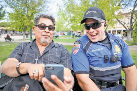  ?? GABRIELA CAMPOS/THE NEW MEXICAN ?? Chris Jaramillo, visiting from Victorvill­e, Calif., shows a photo of his father to Officer Joshua McDermott, aka ‘Officer Smiley,’ while chatting Friday on the Plaza.