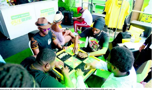  ??  ?? Entertaine­r Bugle (second right) during a game of dominos at the Wray and Nephew White Overproof Rum’s set up.