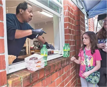  ?? PHOTOS BY ARIEL COBBERT/THE COMMERCIAL APPEAL ?? Volunteer Brad Watkins hands out grab-and-go meals through a window at Caritas Community Center and Cafe in Binghampto­n on Tuesday. Caritas Community Center and Cafe offers free daily meals to out-of-work Memphians.