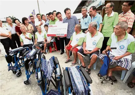  ??  ?? Much needed aid: Kuan (in striped shirt), flanked by MCA Teluk Intan division leaders, handing the mock cheque to Khor (7th from right in green) together with four wheelchair­s to the old folks home.