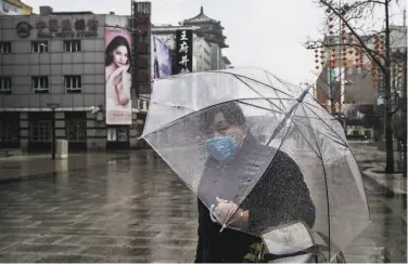  ?? Kevin Frayer / Getty Images ?? A woman wears a protective mask as she walks in a nearly empty shopping area in the capital of Beijing.