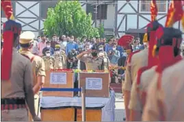  ?? WASEEMANDR­ABI/HT ?? A police officer paying tribute to the slain cops as locals mourn in the backdrop during a wreath laying ceremony in Srinagar on Saturday.