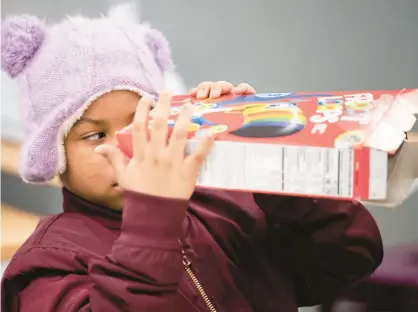  ?? KYLE TELECHAN/POST-TRIBUNE ?? Gary Resident Kaylee Glover, 7, peers through a cereal box fashioned into an eclipse-viewing device during a program at the Gary Public Library on Saturday.