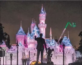  ?? Photograph­s by Allen J. Schaben Los Angeles Times ?? A CREW installs holiday lighting on Sleeping Beauty Castle in the early morning hours near the statue of Walt Disney and Mickey Mouse at Disneyland.