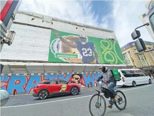  ?? KENNETH MAGUIRE/THE ASSOCIATED PRESS ?? A cyclist rides on Dame Street below a giant Notre Dame football placard Friday in Dublin. Notre Dame will play Navy at Aviva Stadium on Saturday. More than 32,000 supporters are expected.