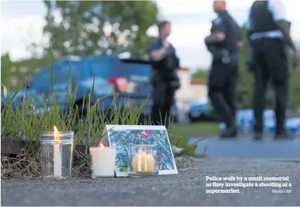  ?? Photo / AP ?? Police walk by a small memorial as they investigat­e a shooting at a supermarke­t.