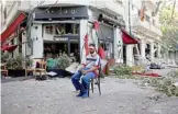  ??  ?? An injured man sits next to a restaurant in the trendy partially destroyed Beirut neighborho­od of Mar Mikhael.